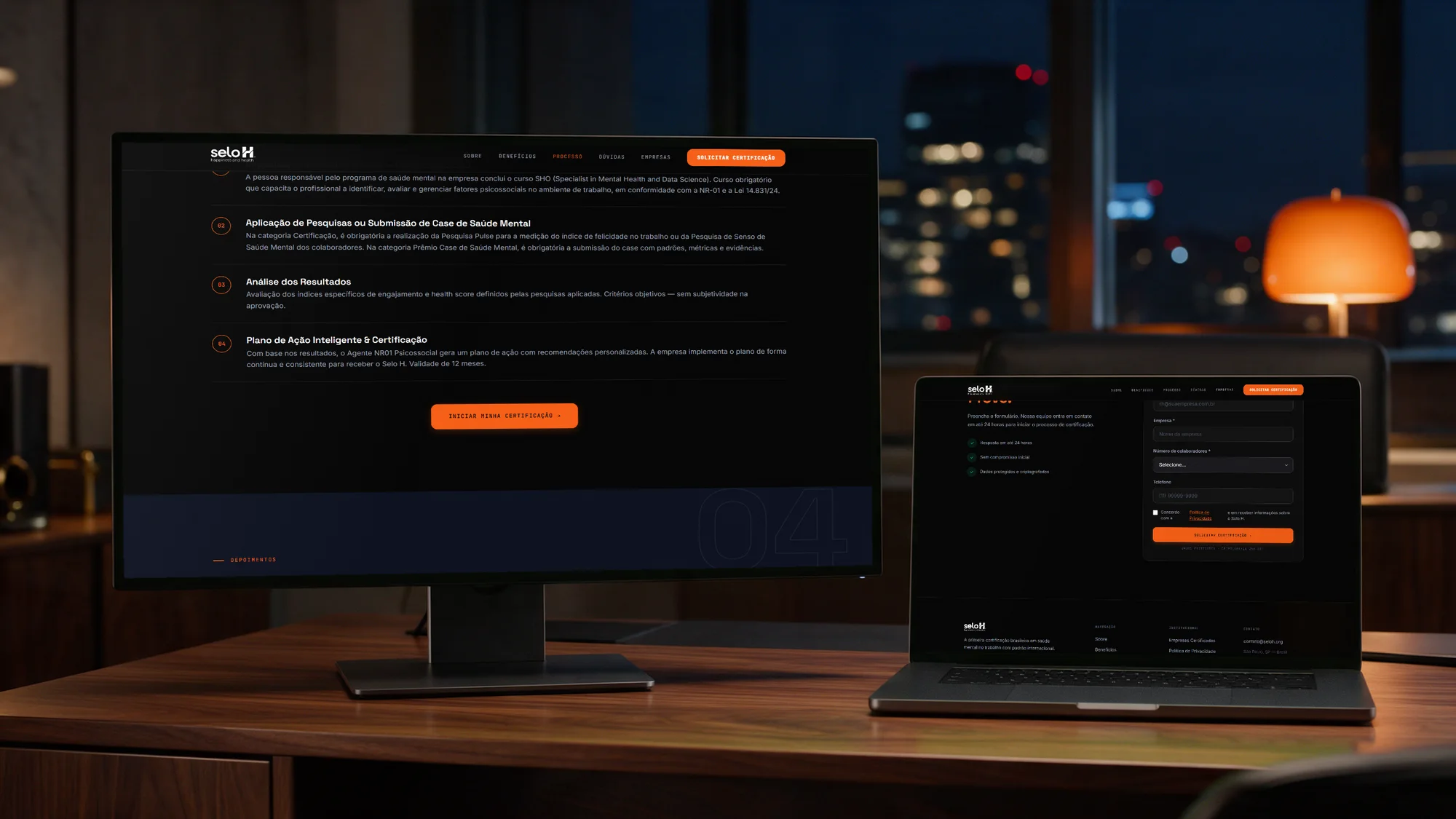 The rebuilt Selo H site on a monitor and laptop in an office at night